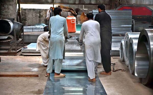 Workers manually unroll steel coils to produce door frames in Karachi