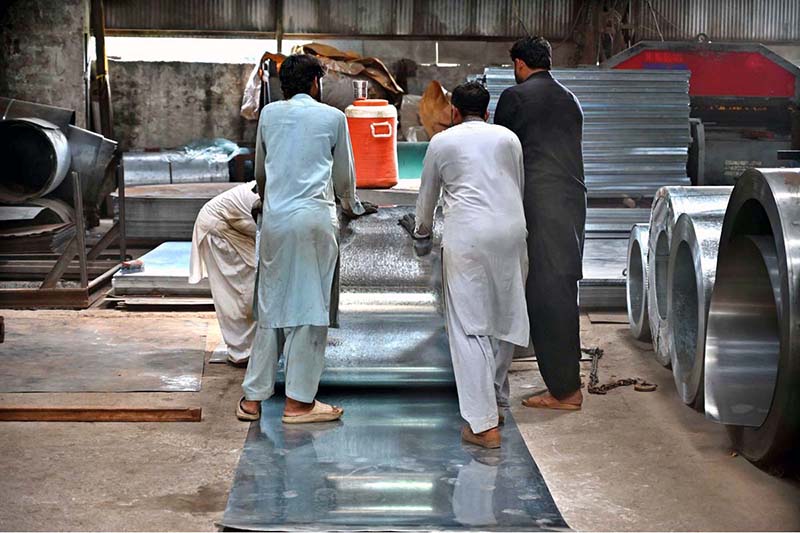 Workers manually unroll steel coils to produce door frames in Karachi